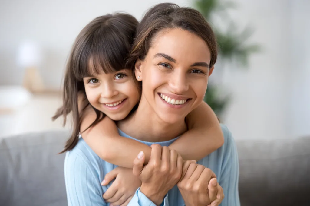 Mother smiling while her daughter hugs her from behind